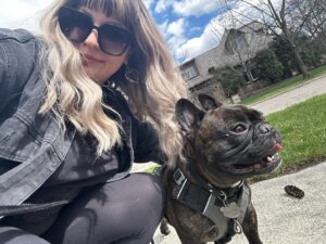 Olivia, a dog walker from Hands N Paws, smiles while walking a happy dog on a leash in a Columbus park, demonstrating her commitment to excellent pet care.